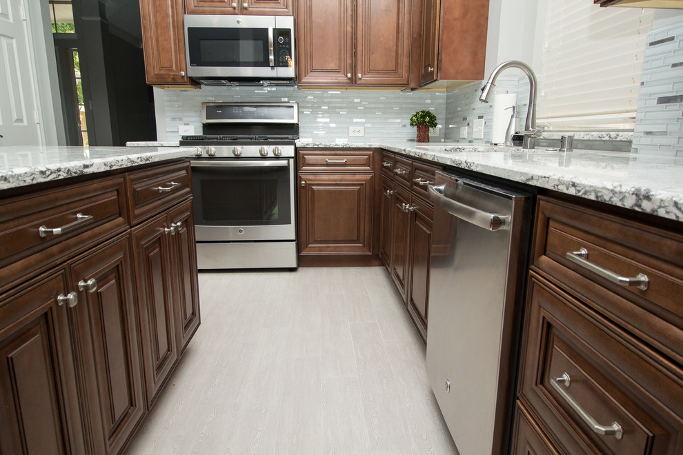 Example of a mid-sized transitional l-shaped porcelain tile and gray floor kitchen design in Houston with a single-bowl sink, raised-panel cabinets, medium tone wood cabinets, quartz countertops, gray backsplash, mosaic tile backsplash, stainless steel appliances and two islands