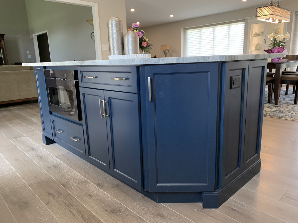Example of a large transitional l-shaped vinyl floor and gray floor eat-in kitchen design with an undermount sink, recessed-panel cabinets, white cabinets, quartz countertops, gray backsplash, ceramic backsplash, stainless steel appliances, an island and white countertops