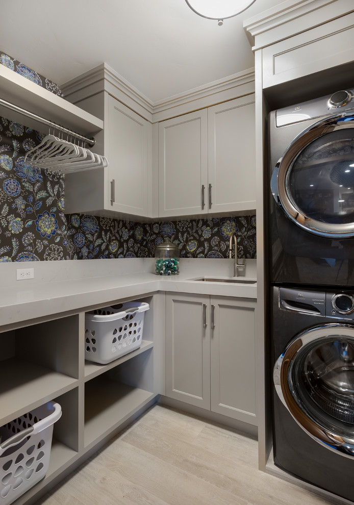 Photo of a mid-sized country dedicated laundry room in Salt Lake City with recessed-panel cabinets, grey cabinets, quartz benchtops, multi-coloured walls, a stacked washer and dryer, grey benchtop, an undermount sink, light hardwood floors and beige floor.
