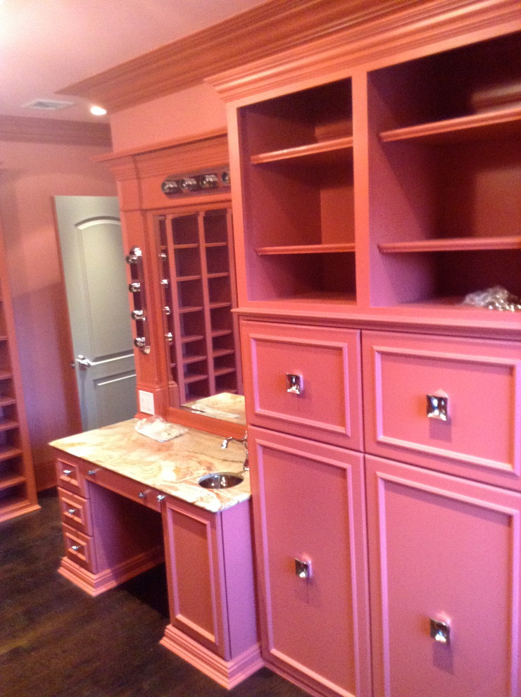 Photo of a large modern women's dressing room in New York with raised-panel cabinets, red cabinets and dark hardwood floors.
