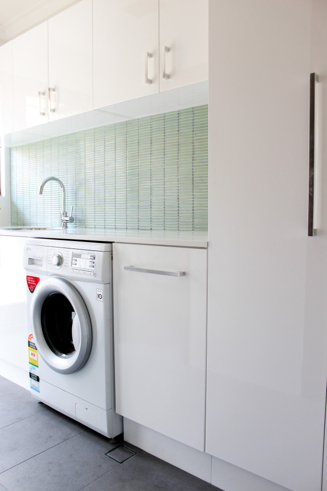 This is an example of a small modern single-wall dedicated laundry room in Perth with a drop-in sink, flat-panel cabinets, white cabinets, quartz benchtops, green walls, porcelain floors, an integrated washer and dryer, grey floor and white benchtop.
