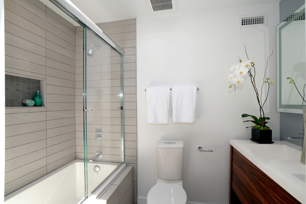 This is an example of a small modern master bathroom in San Francisco with flat-panel cabinets, dark wood cabinets, an alcove tub, a shower/bathtub combo, a one-piece toilet, beige tile, an integrated sink, glass benchtops, a sliding shower screen, white benchtops and white walls.