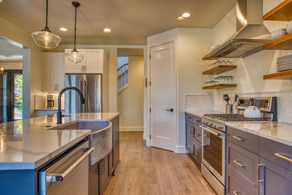 This is an example of a mid-sized country galley open plan kitchen in Salt Lake City with a farmhouse sink, shaker cabinets, blue cabinets, quartzite benchtops, white splashback, ceramic splashback, stainless steel appliances, medium hardwood floors, with island, brown floor and white benchtop.