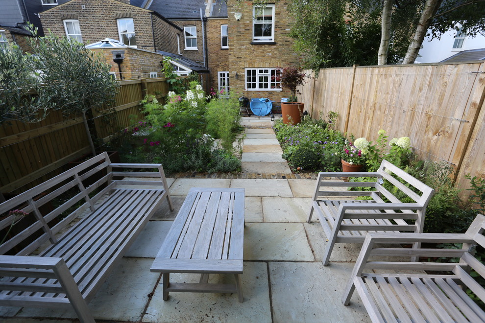 This is an example of a small country backyard patio in London with natural stone pavers.