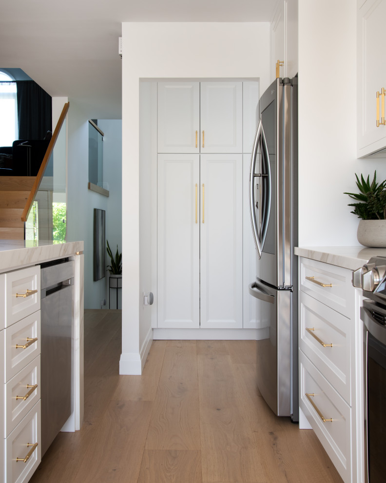 Mid-sized transitional galley light wood floor and beige floor open concept kitchen photo in Ottawa with an undermount sink, recessed-panel cabinets, white cabinets, quartz countertops, white backsplash, porcelain backsplash, stainless steel appliances, an island and white countertops