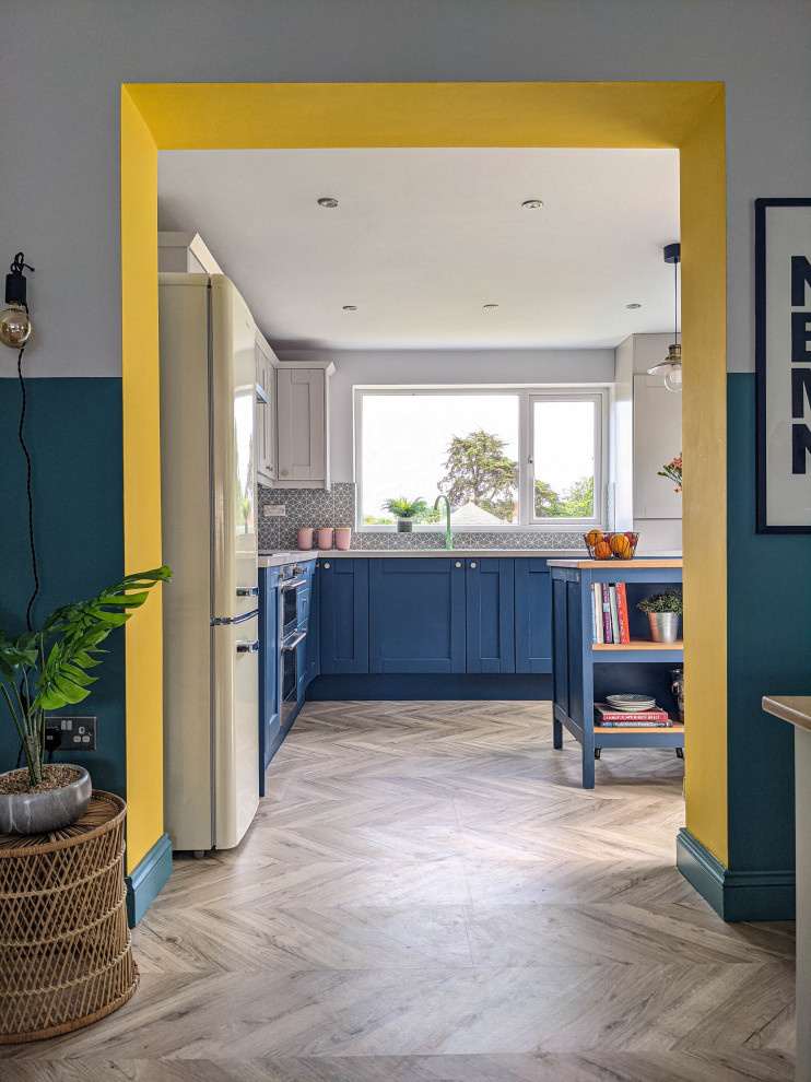 Mid-sized beach style l-shaped open plan kitchen in Other with an integrated sink, shaker cabinets, blue cabinets, laminate benchtops, grey splashback, ceramic splashback, black appliances, laminate floors, with island and grey benchtop.