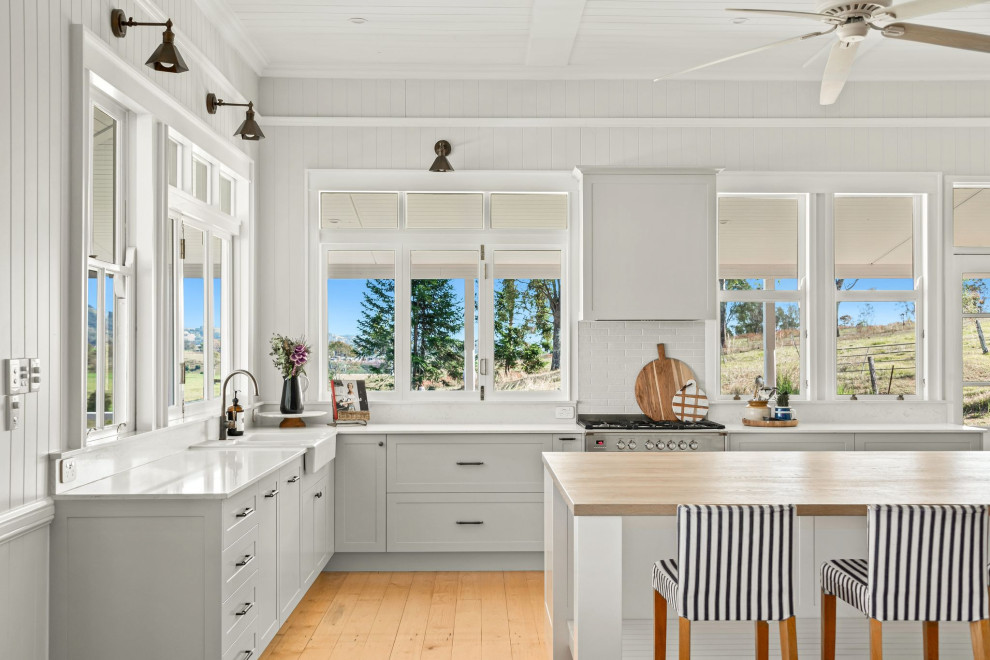 Photo of a mid-sized country l-shaped kitchen pantry in Sunshine Coast with a farmhouse sink, shaker cabinets, green cabinets, quartz benchtops, white splashback, engineered quartz splashback, stainless steel appliances, medium hardwood floors, with island, yellow floor, white benchtop and timber.