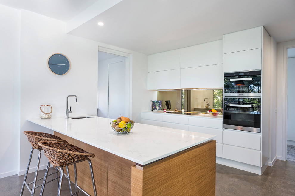 Design ideas for a large beach style galley eat-in kitchen in Sunshine Coast with an undermount sink, white cabinets, mirror splashback, stainless steel appliances, concrete floors and with island.
