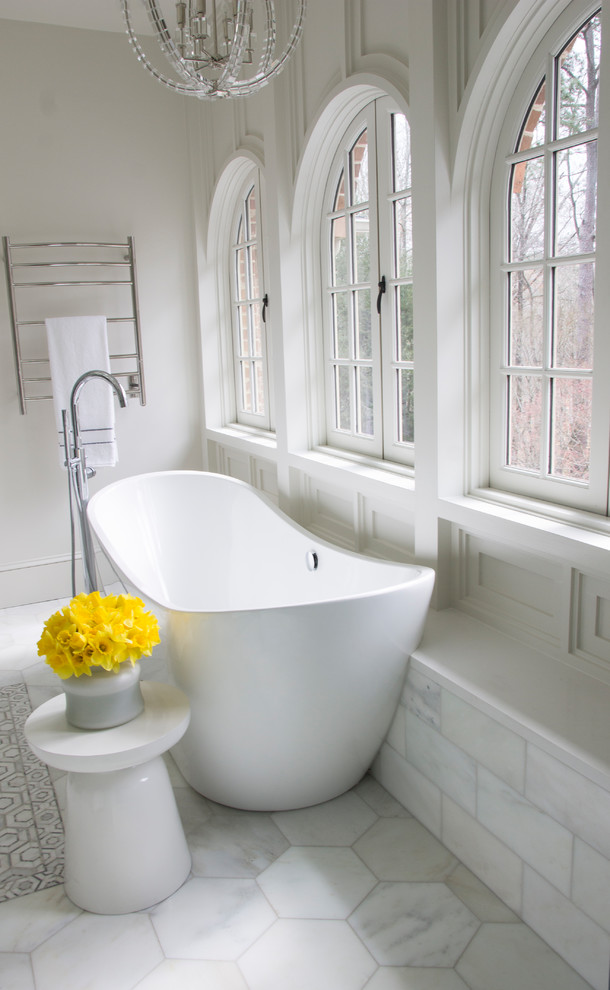 This is an example of a mid-sized transitional master bathroom in Atlanta with white cabinets, a freestanding tub, an alcove shower, a wall-mount toilet, white tile, marble, white walls, marble floors, an undermount sink, engineered quartz benchtops, white floor, a hinged shower door and white benchtops.