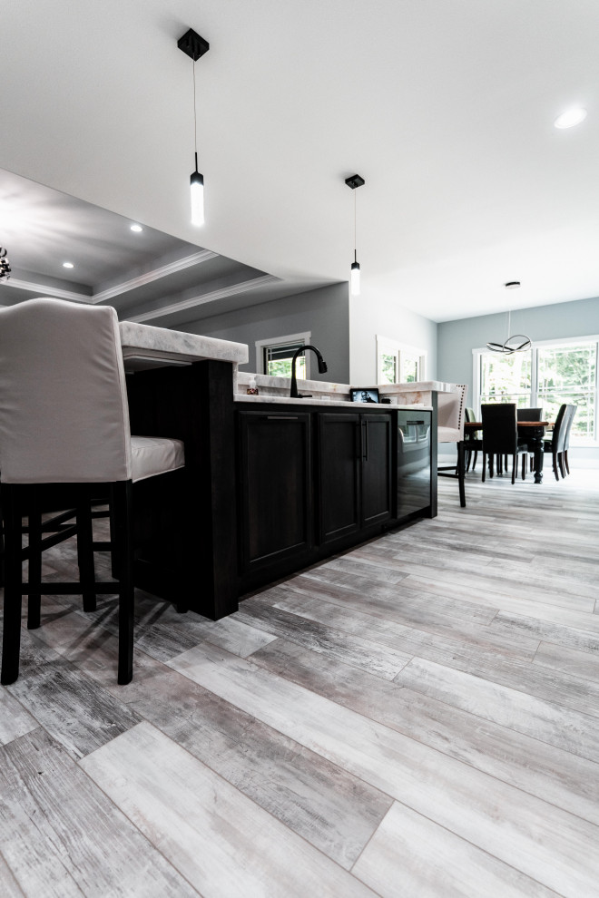 Open concept kitchen - huge transitional l-shaped laminate floor, gray floor and tray ceiling open concept kitchen idea with an undermount sink, flat-panel cabinets, white cabinets, quartz countertops, gray backsplash, ceramic backsplash, black appliances and an island