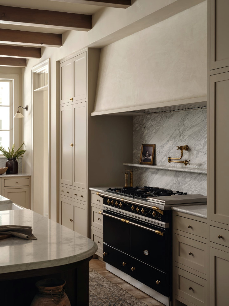 Transitional l-shaped medium tone wood floor, brown floor and exposed beam kitchen photo in Austin with a farmhouse sink, shaker cabinets, beige cabinets, gray backsplash, black appliances, an island and gray countertops