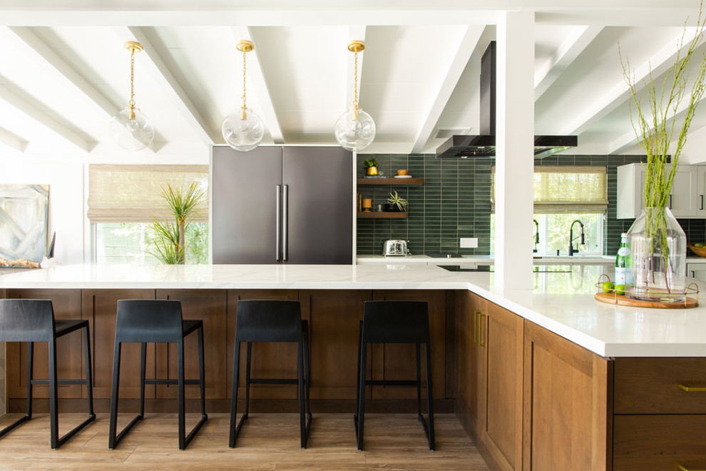 Design ideas for a midcentury l-shaped kitchen in Los Angeles with an undermount sink, shaker cabinets, medium wood cabinets, green splashback, stainless steel appliances, medium hardwood floors, with island, brown floor and white benchtop.