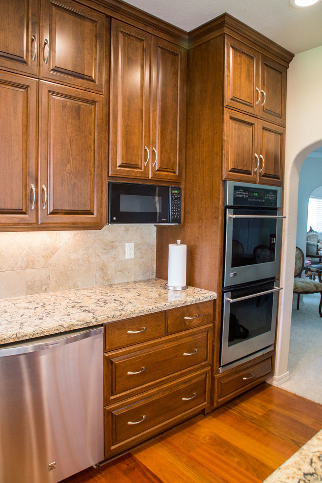 Photo of a traditional u-shaped kitchen in Sacramento with an undermount sink, raised-panel cabinets, brown cabinets, quartz benchtops, beige splashback, white appliances, medium hardwood floors and with island.