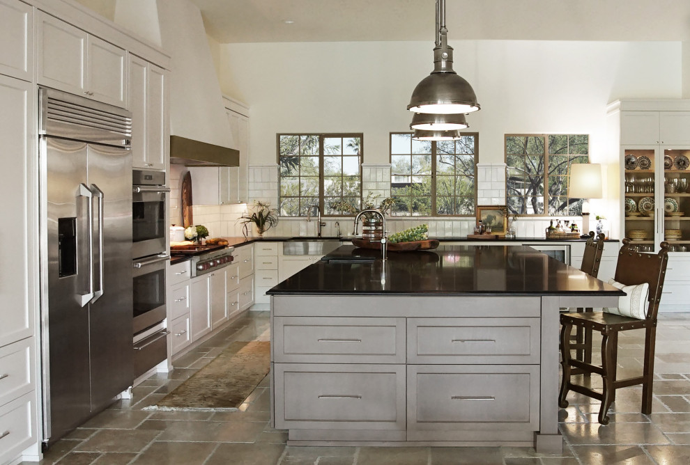 This is an example of a large transitional l-shaped eat-in kitchen in Phoenix with an integrated sink, recessed-panel cabinets, white cabinets, granite benchtops, white splashback, ceramic splashback, stainless steel appliances, limestone floors, with island, beige floor, black benchtop and coffered.