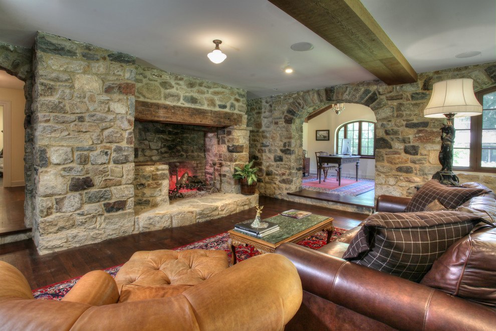 Photo of a country enclosed living room in New York with a stone fireplace surround and dark hardwood floors.