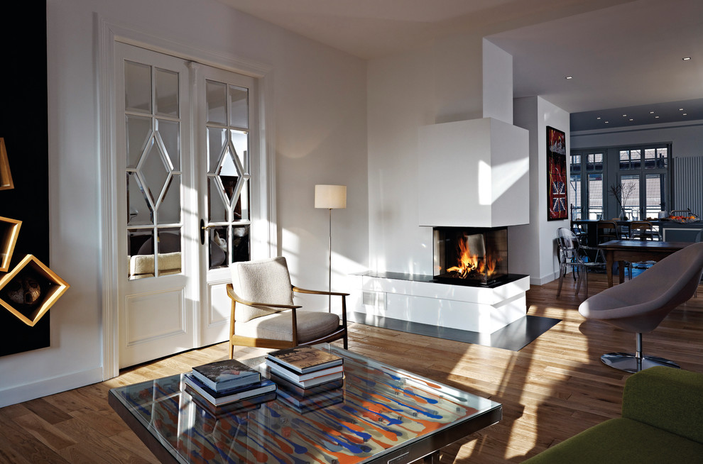 This is an example of a mid-sized contemporary open concept living room in Munich with white walls, medium hardwood floors, a two-sided fireplace and a plaster fireplace surround.