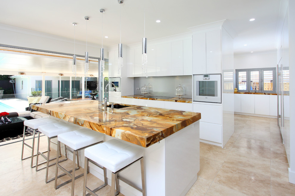 This is an example of a mid-sized contemporary galley open plan kitchen in Brisbane with an undermount sink, flat-panel cabinets, white cabinets, grey splashback, glass sheet splashback, white appliances, quartz benchtops, porcelain floors, with island, beige floor and multi-coloured benchtop.
