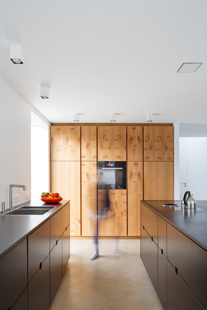 Contemporary galley open plan kitchen in Cologne with a drop-in sink, flat-panel cabinets, dark wood cabinets, quartzite benchtops, white splashback, timber splashback, terrazzo floors, with island and grey floor.