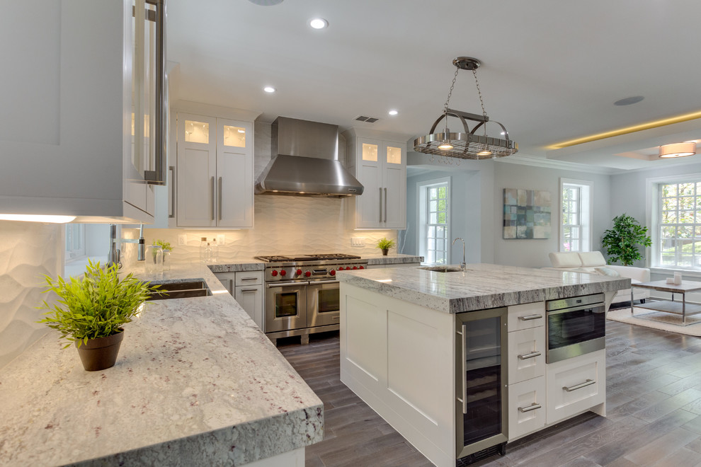 Example of a large transitional l-shaped medium tone wood floor open concept kitchen design in DC Metro with a single-bowl sink, shaker cabinets, white cabinets, marble countertops, white backsplash, porcelain backsplash, stainless steel appliances and an island