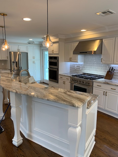 Inspiration for a large transitional l-shaped medium tone wood floor and brown floor open concept kitchen remodel with a farmhouse sink, raised-panel cabinets, white cabinets, granite countertops, white backsplash, ceramic backsplash, stainless steel appliances, an island and gray countertops