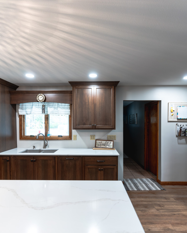Example of a huge transitional l-shaped medium tone wood floor and brown floor open concept kitchen design with shaker cabinets, medium tone wood cabinets, quartz countertops, stainless steel appliances, an island and white countertops