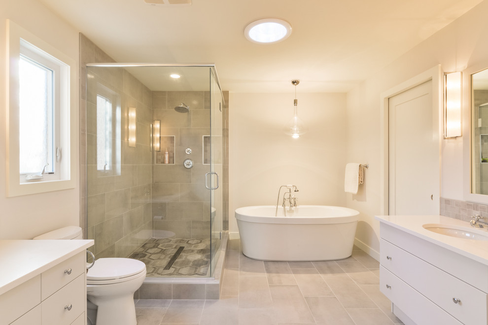 Photo of a mid-sized contemporary master bathroom in Orange County with flat-panel cabinets, white cabinets, a freestanding tub, an alcove shower, gray tile, porcelain tile, white walls, porcelain floors, an undermount sink, solid surface benchtops, grey floor and a hinged shower door.