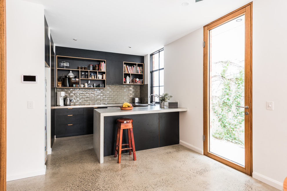Photo of a contemporary l-shaped kitchen in Melbourne with flat-panel cabinets, black cabinets, grey splashback, subway tile splashback, concrete floors, a peninsula, grey floor and white benchtop.