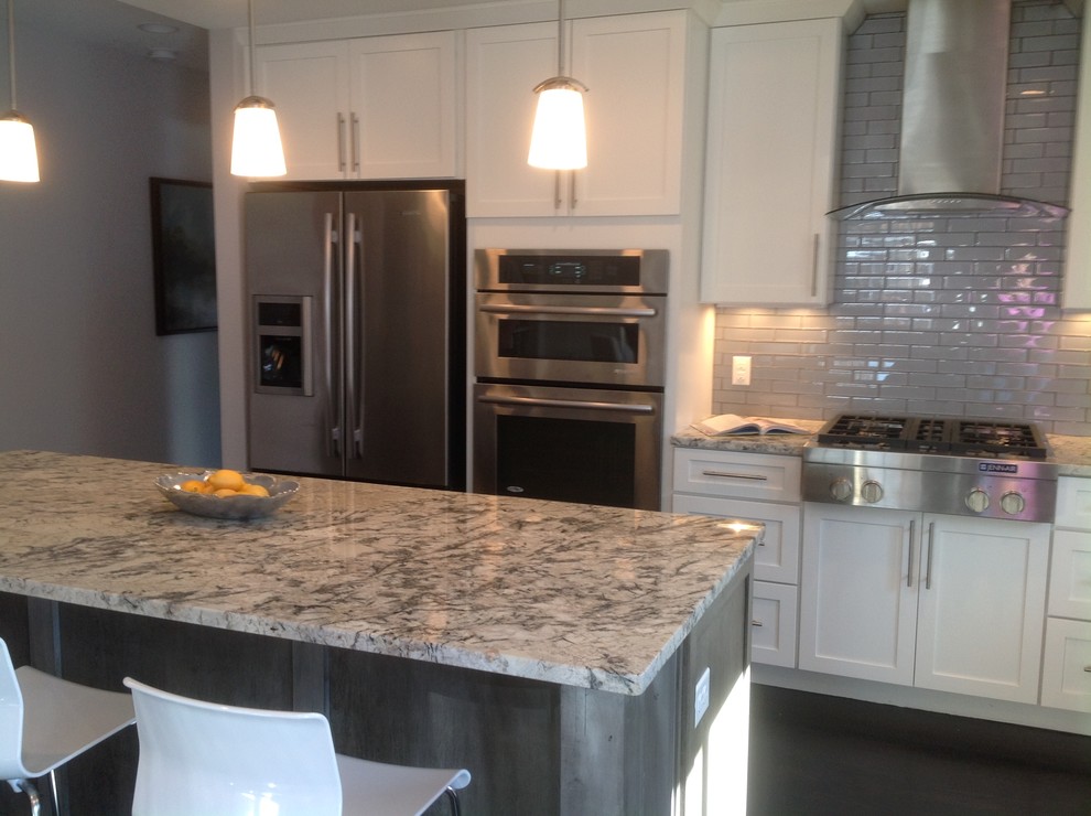 This is an example of a mid-sized transitional galley eat-in kitchen in Denver with a double-bowl sink, recessed-panel cabinets, white cabinets, granite benchtops, grey splashback, ceramic splashback, stainless steel appliances, dark hardwood floors and with island.