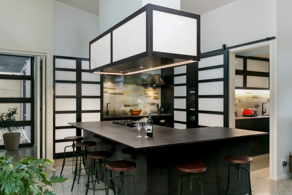 This is an example of a mid-sized asian l-shaped kitchen pantry in Adelaide with a drop-in sink, dark wood cabinets, solid surface benchtops, multi-coloured splashback, glass sheet splashback, panelled appliances, concrete floors, with island, grey floor and black benchtop.