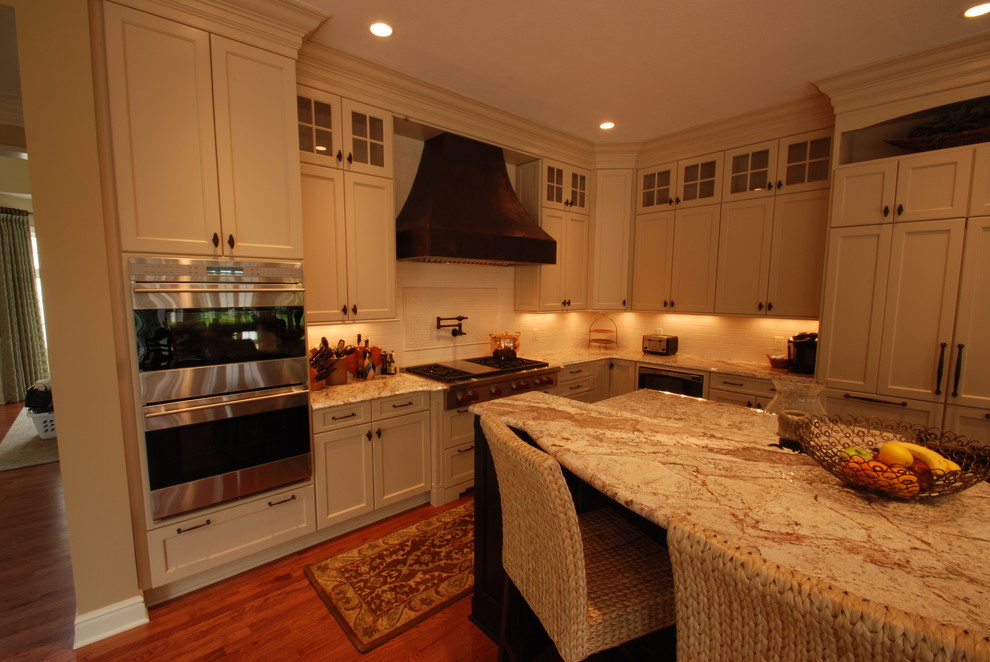 Eat-in kitchen - large transitional l-shaped medium tone wood floor eat-in kitchen idea with a farmhouse sink, recessed-panel cabinets, light wood cabinets, granite countertops, white backsplash, ceramic backsplash, stainless steel appliances and an island