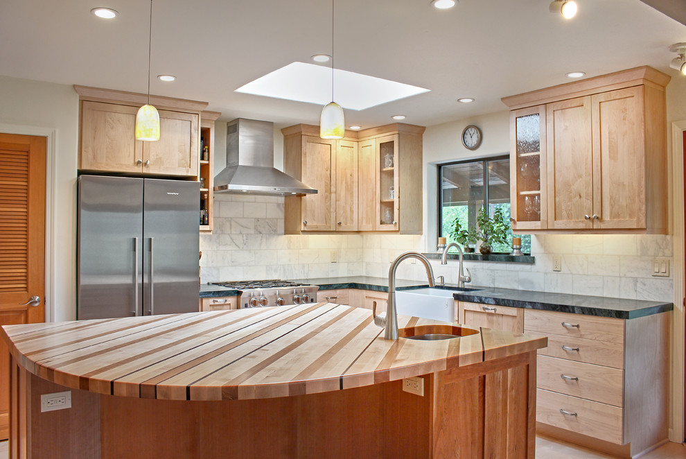 Eat-in kitchen - mid-sized transitional l-shaped light wood floor and brown floor eat-in kitchen idea with a farmhouse sink, shaker cabinets, light wood cabinets, wood countertops, white backsplash, marble backsplash, stainless steel appliances and an island