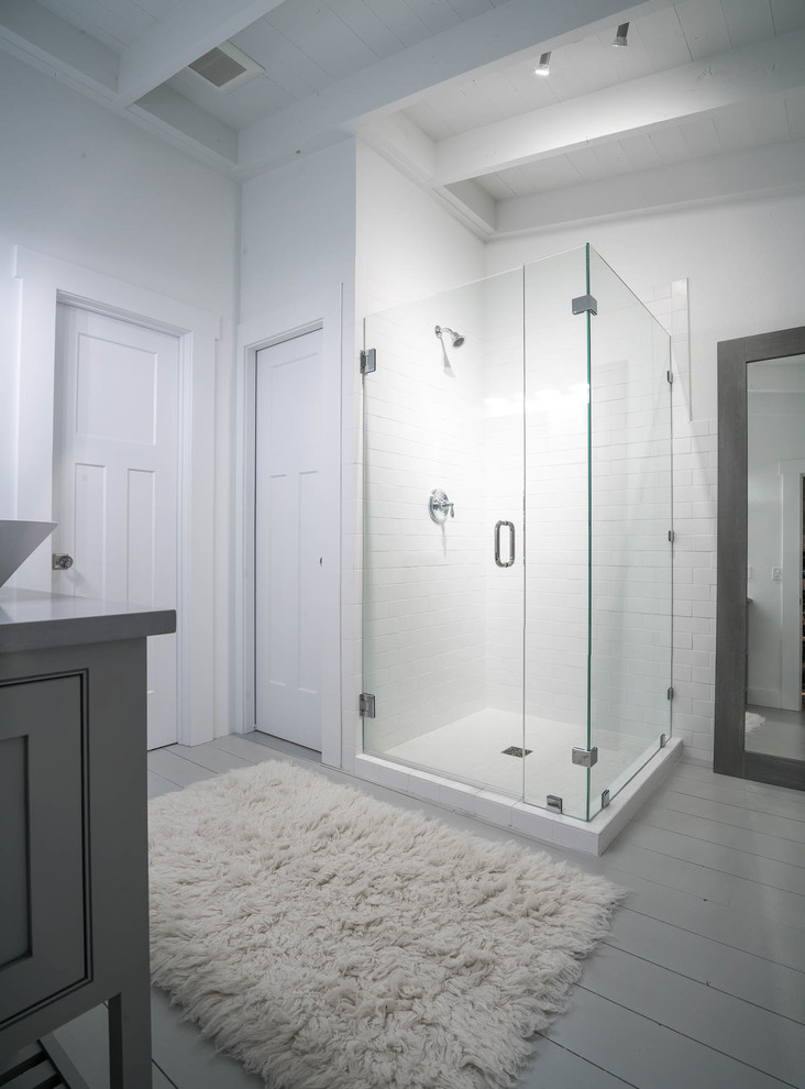 This is an example of a mid-sized beach style master bathroom in Other with beaded inset cabinets, grey cabinets, a corner shower, a two-piece toilet, white tile, subway tile, white walls, painted wood floors, a vessel sink, engineered quartz benchtops, white floor and a hinged shower door.