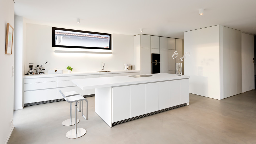 This is an example of an expansive contemporary open plan kitchen in Berlin with an undermount sink, flat-panel cabinets, white cabinets, white splashback, black appliances and with island.