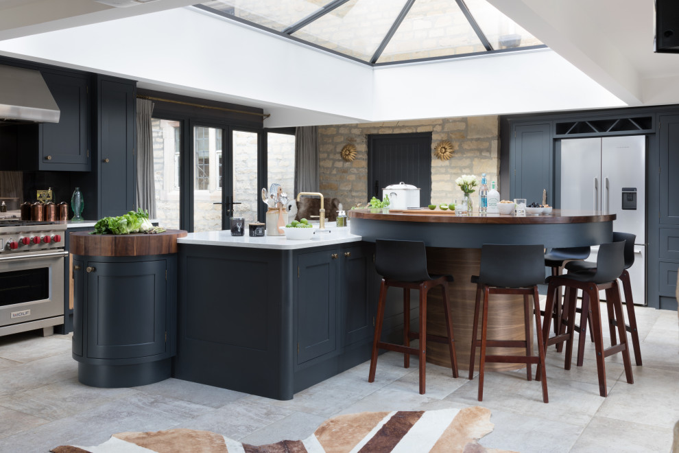 Photo of a large transitional single-wall open plan kitchen in Other with a farmhouse sink, shaker cabinets, blue cabinets, marble benchtops, brown splashback, mirror splashback, stainless steel appliances, porcelain floors, with island, beige floor and white benchtop.