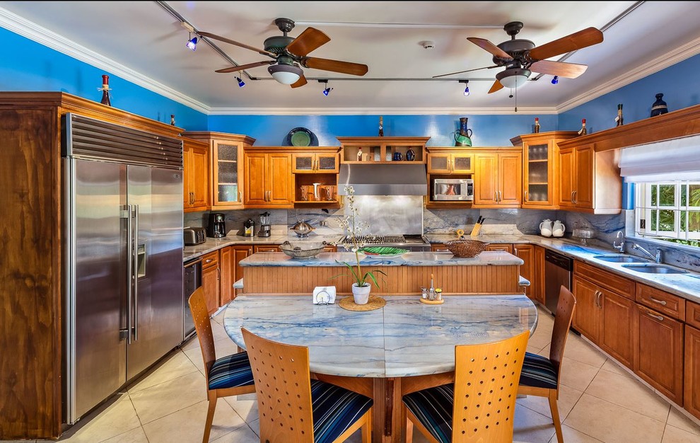 Large tropical u-shaped kitchen in Other with a double-bowl sink, raised-panel cabinets, medium wood cabinets, marble benchtops, blue splashback, marble splashback, stainless steel appliances, porcelain floors, with island, beige floor and blue benchtop.