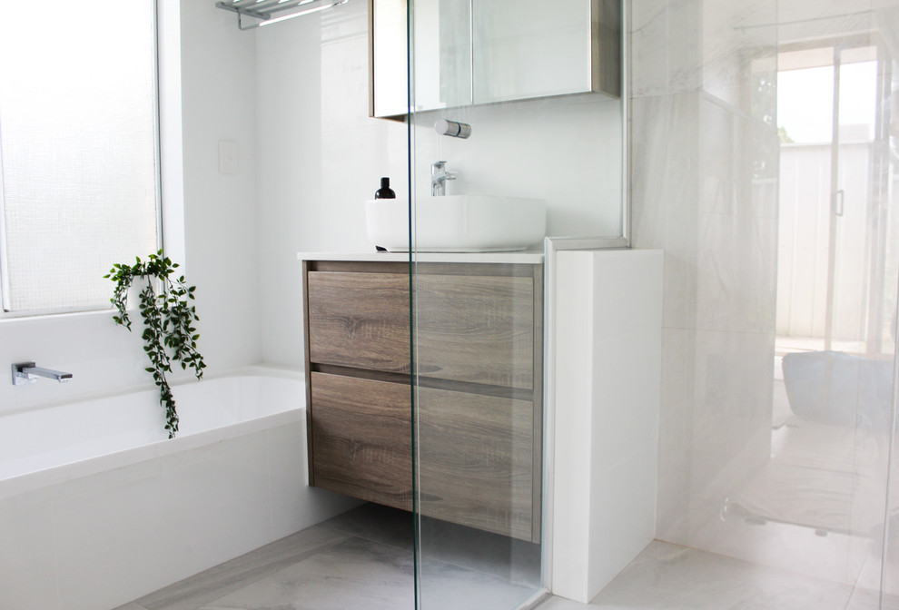 This is an example of a mid-sized modern kids bathroom in Perth with flat-panel cabinets, brown cabinets, a drop-in tub, a corner shower, white tile, ceramic tile, white walls, porcelain floors, a vessel sink, engineered quartz benchtops, grey floor, a hinged shower door and white benchtops.