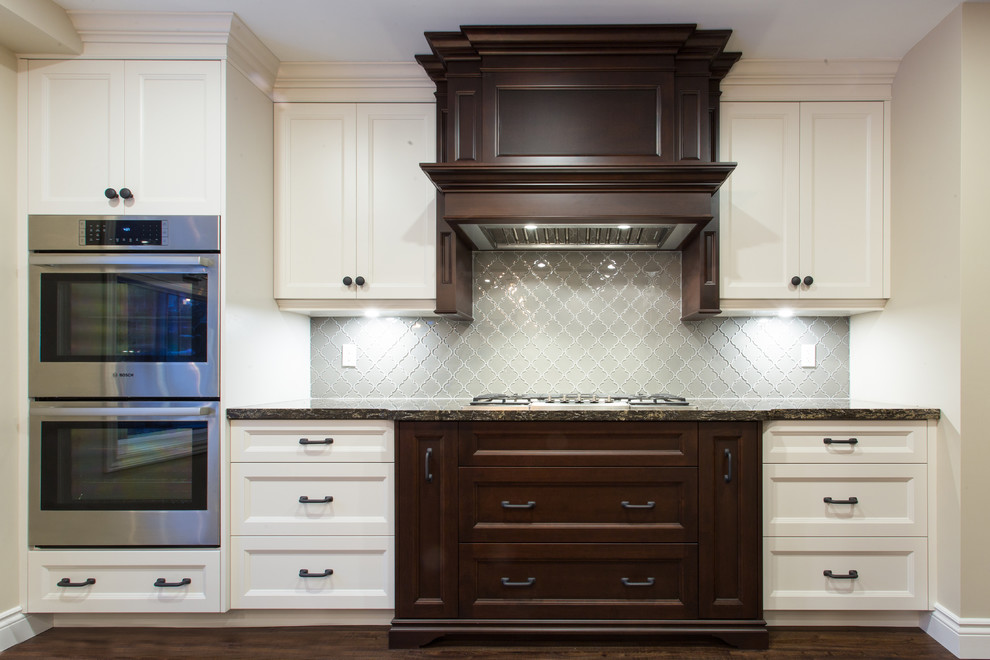 Inspiration for a large transitional l-shaped dark wood floor eat-in kitchen remodel in Orange County with a double-bowl sink, recessed-panel cabinets, white cabinets, granite countertops, gray backsplash, glass tile backsplash, stainless steel appliances and an island