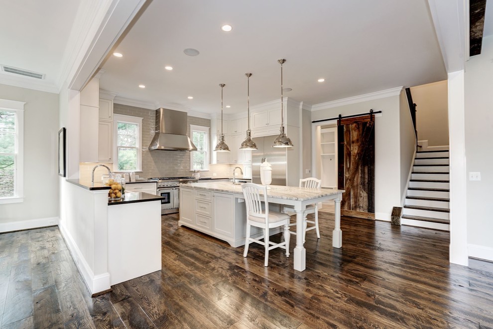 Inspiration for a large country u-shaped open plan kitchen in DC Metro with a farmhouse sink, recessed-panel cabinets, white cabinets, granite benchtops, brown splashback, subway tile splashback, stainless steel appliances, dark hardwood floors, with island and brown floor.