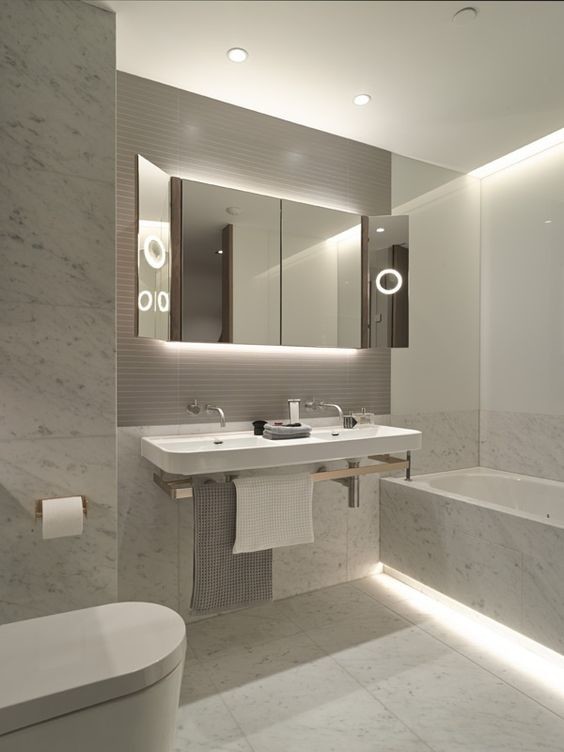 Photo of a mid-sized modern master bathroom in New York with white cabinets, a drop-in tub, a wall-mount toilet, white tile, stone slab, white walls, marble floors, a wall-mount sink, solid surface benchtops, white floor and white benchtops.