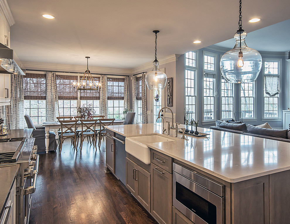 Photo of a large transitional l-shaped open plan kitchen in Atlanta with a farmhouse sink, shaker cabinets, white cabinets, quartzite benchtops, white splashback, subway tile splashback, stainless steel appliances, medium hardwood floors, with island and brown floor.
