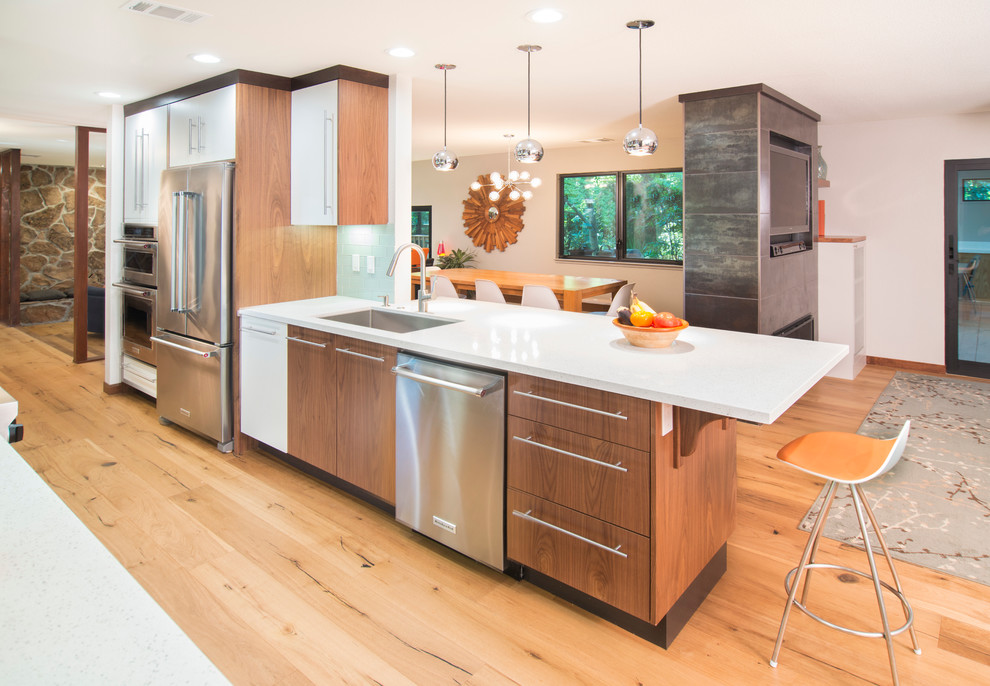 This is an example of a mid-sized contemporary galley separate kitchen in San Francisco with an undermount sink, flat-panel cabinets, medium wood cabinets, glass benchtops, green splashback, glass tile splashback, stainless steel appliances, light hardwood floors and a peninsula.