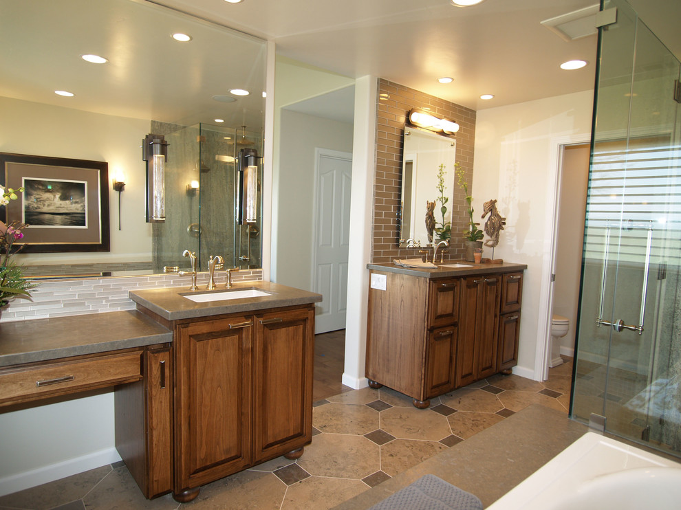 This is an example of a mid-sized transitional master bathroom in Sacramento with an undermount sink, raised-panel cabinets, medium wood cabinets, limestone benchtops, a drop-in tub, a double shower, a one-piece toilet, multi-coloured tile, glass tile, beige walls and limestone floors.