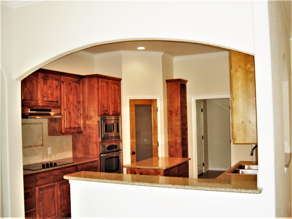 Example of a mid-sized classic u-shaped eat-in kitchen design with a drop-in sink, raised-panel cabinets, medium tone wood cabinets, granite countertops, beige backsplash, ceramic backsplash, stainless steel appliances, an island and multicolored countertops