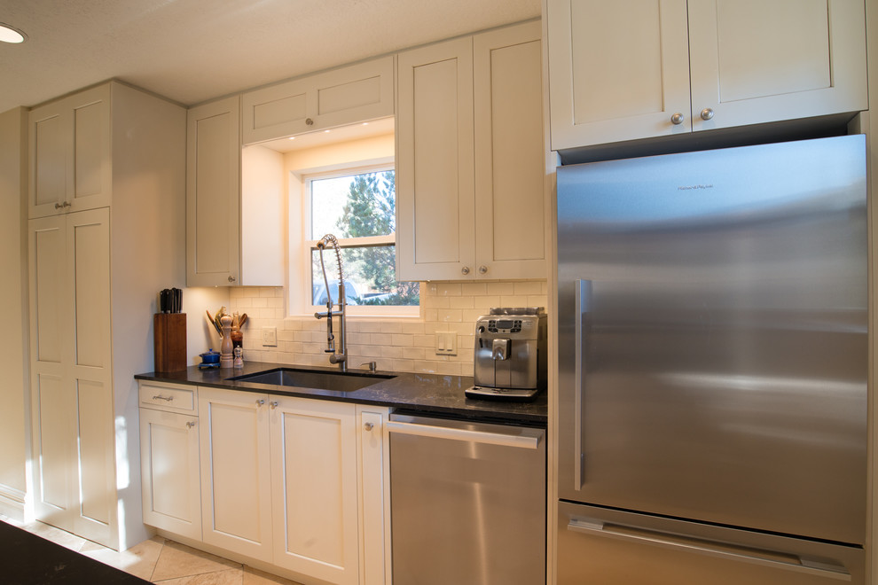 Inspiration for a small transitional galley limestone floor and beige floor open concept kitchen remodel in Albuquerque with an undermount sink, shaker cabinets, white cabinets, solid surface countertops, white backsplash, subway tile backsplash, stainless steel appliances and a peninsula