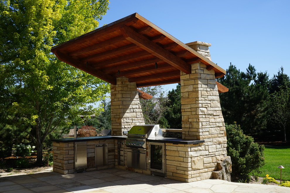 This is an example of a mid-sized country backyard patio in Denver with an outdoor kitchen and natural stone pavers.