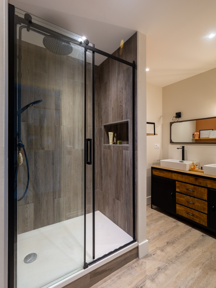 This is an example of a mid-sized industrial master bathroom in Lyon with beaded inset cabinets, dark wood cabinets, an alcove shower, gray tile, wood-look tile, beige walls, wood-look tile, a drop-in sink, wood benchtops, a sliding shower screen, a laundry, a double vanity and a freestanding vanity.