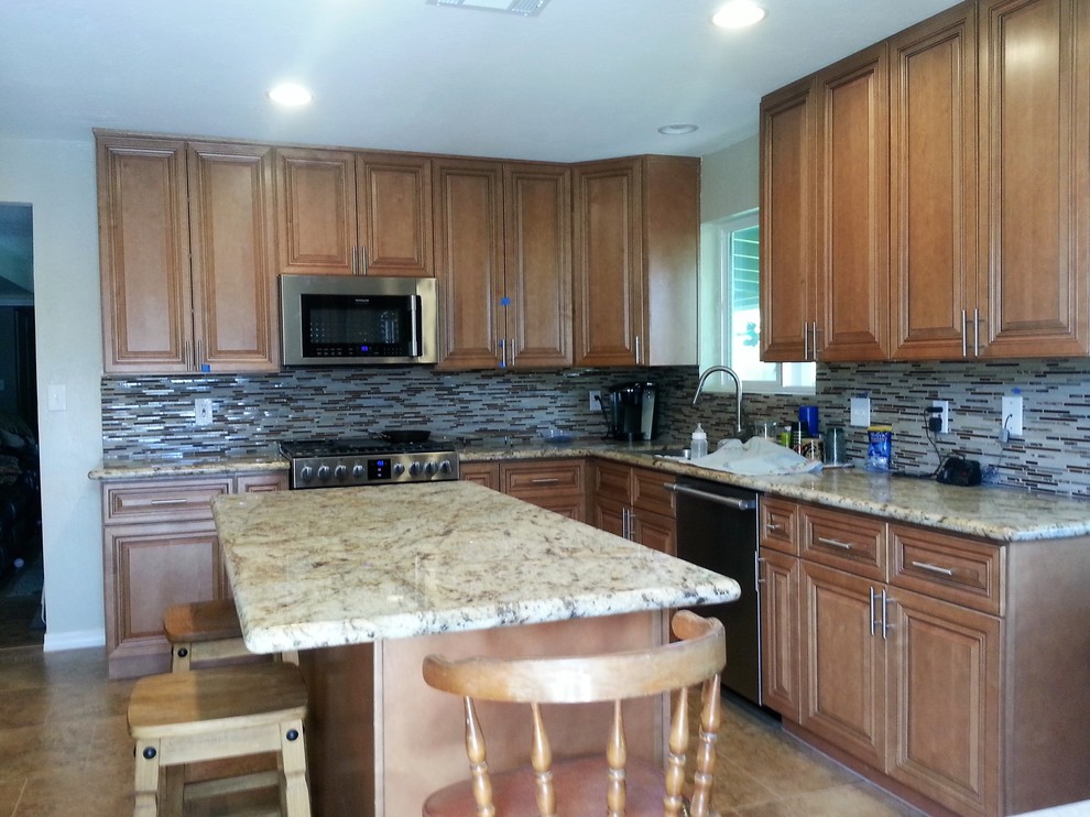 Transitional l-shaped ceramic tile eat-in kitchen photo in Phoenix with an undermount sink, raised-panel cabinets, medium tone wood cabinets, granite countertops, multicolored backsplash, glass tile backsplash, stainless steel appliances and an island