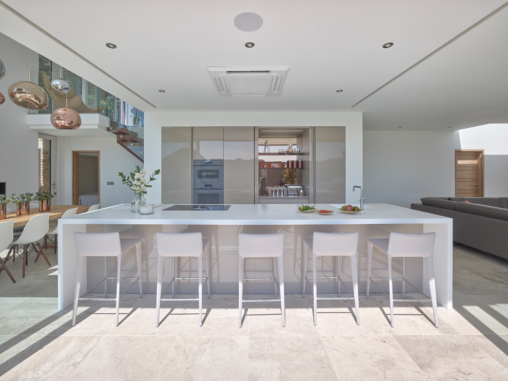 Photo of a large contemporary single-wall open plan kitchen in Other with flat-panel cabinets, beige cabinets, solid surface benchtops, mirror splashback, limestone floors, with island, beige floor and white benchtop.