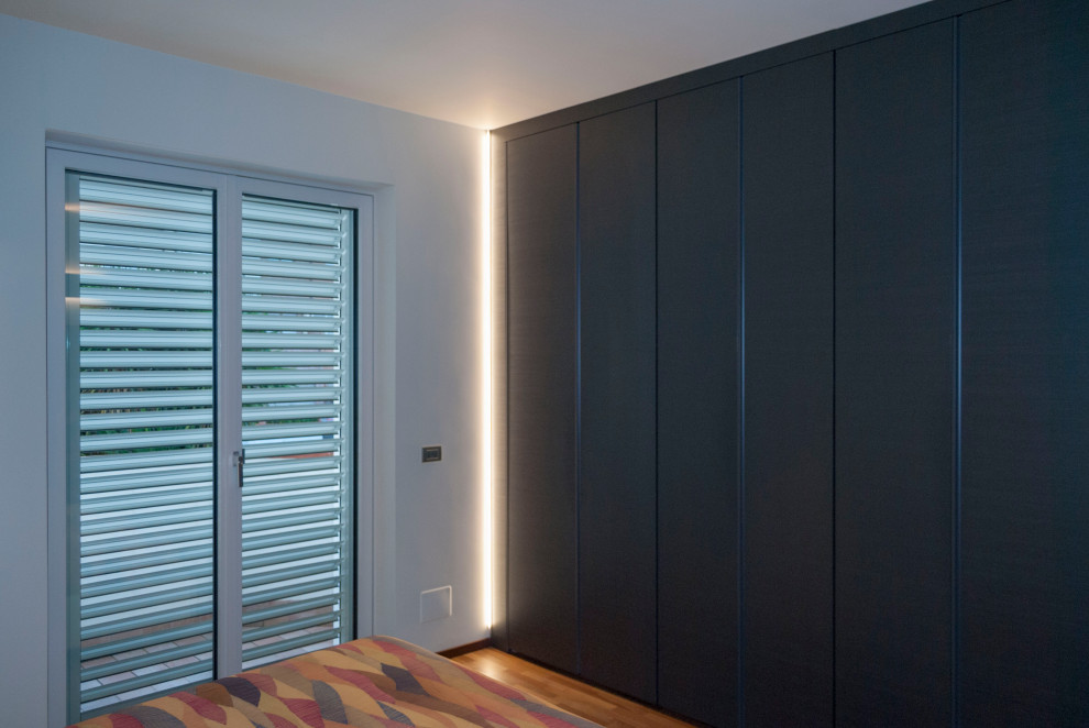 Photo of a large modern gender neutral standard wardrobe in Other with flat-panel cabinets, black cabinets and light hardwood flooring.