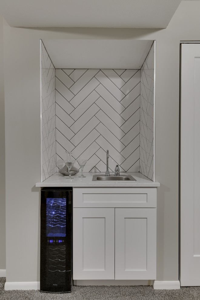 Inspiration for a small transitional galley wet bar in Minneapolis with a drop-in sink, shaker cabinets, white cabinets, quartz benchtops, white splashback, ceramic splashback, carpet, grey floor and white benchtop.